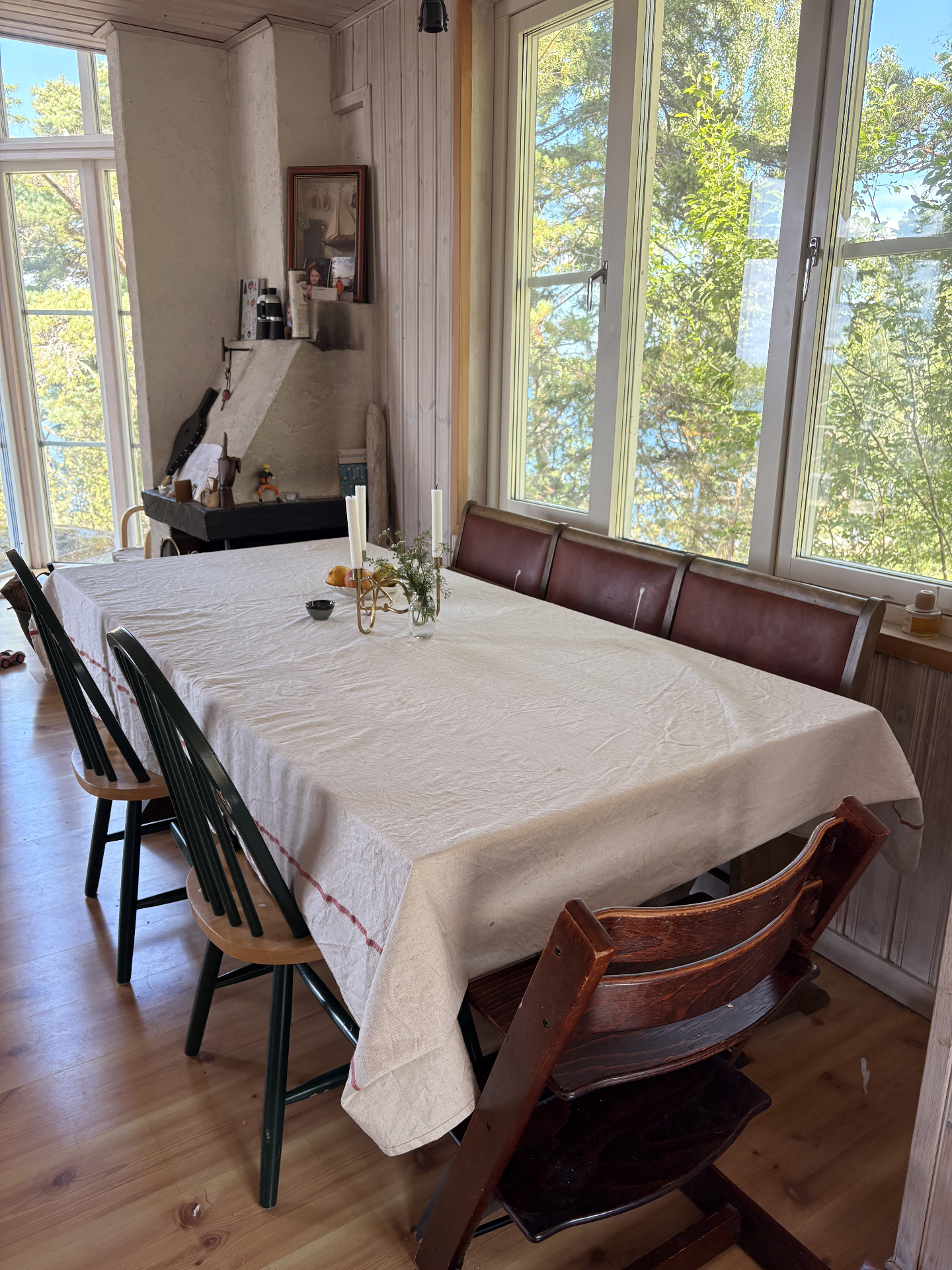 Långt matbord dukat i linne, höga fönster mot tallarna och havet